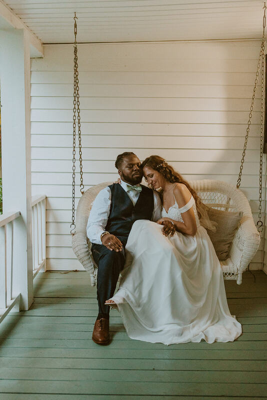 bride and groom sitting on white wicker porch swing