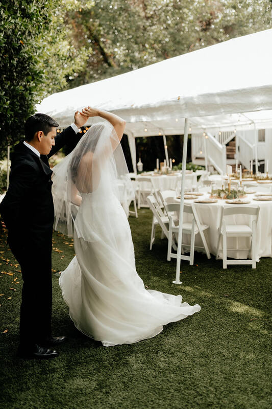 groom twirling bride next to tented wedding reception