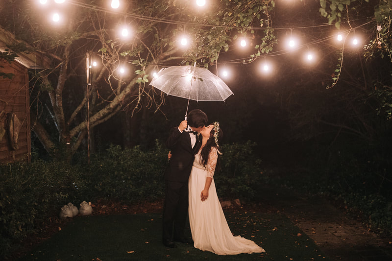 bride and groom kissing at night under clear umbrella