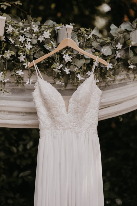 wedding dress hanging on arbor decorated with greenery