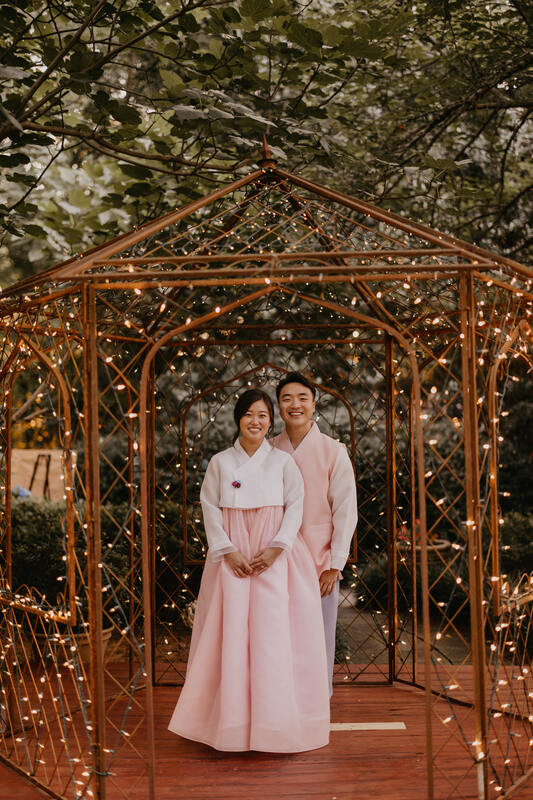 bride and groom posing in garden gazebo wearing Korean hanbok