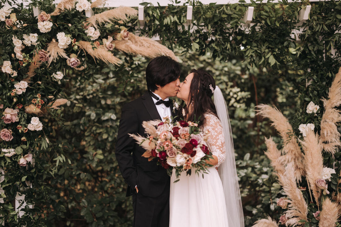 bride and groom kissing at boho altar with pampas grass