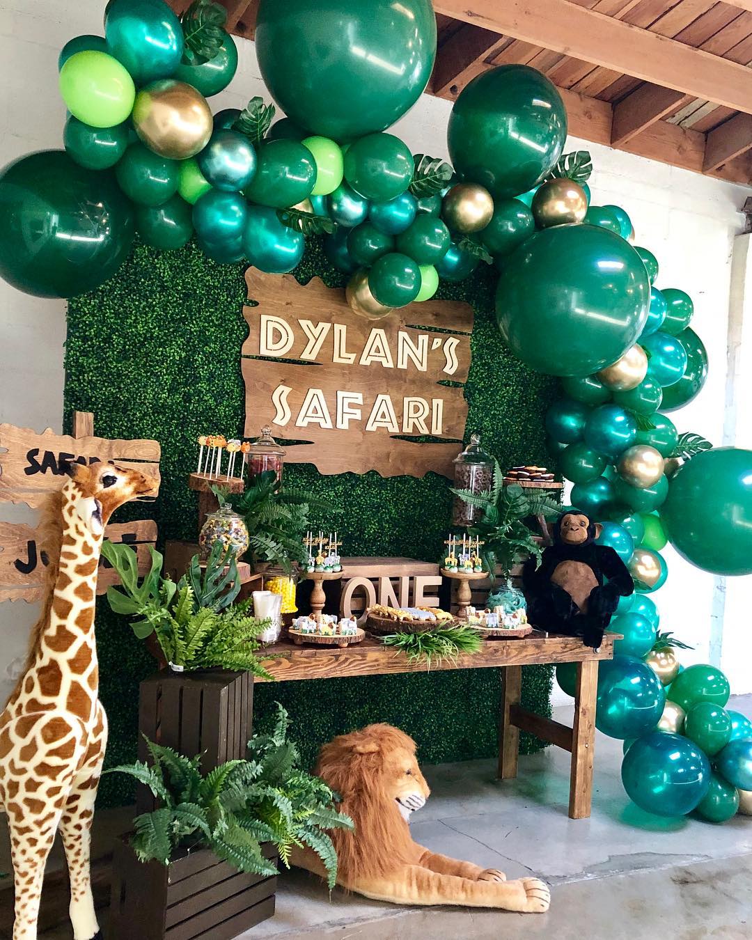 Safari themed birthday party for boy's 1st birthday. Decorated with turf grass wall, large stuffed animals, and green and gold balloons.