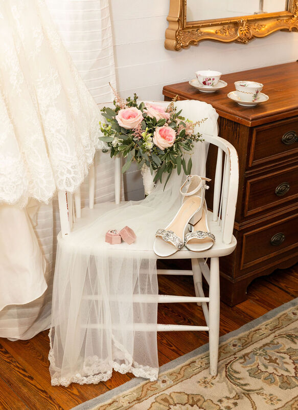 detail photo of bride's shoes, rings, bouquet, and veil on antique white chair