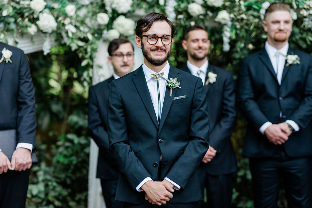 groom at altar with greenery and white florals