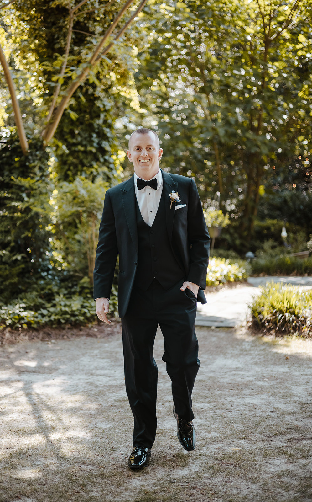 groom in black tux walking through garden venue