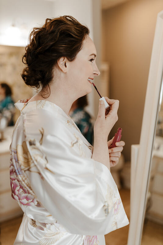 bride in silk white robe putting on lipstick