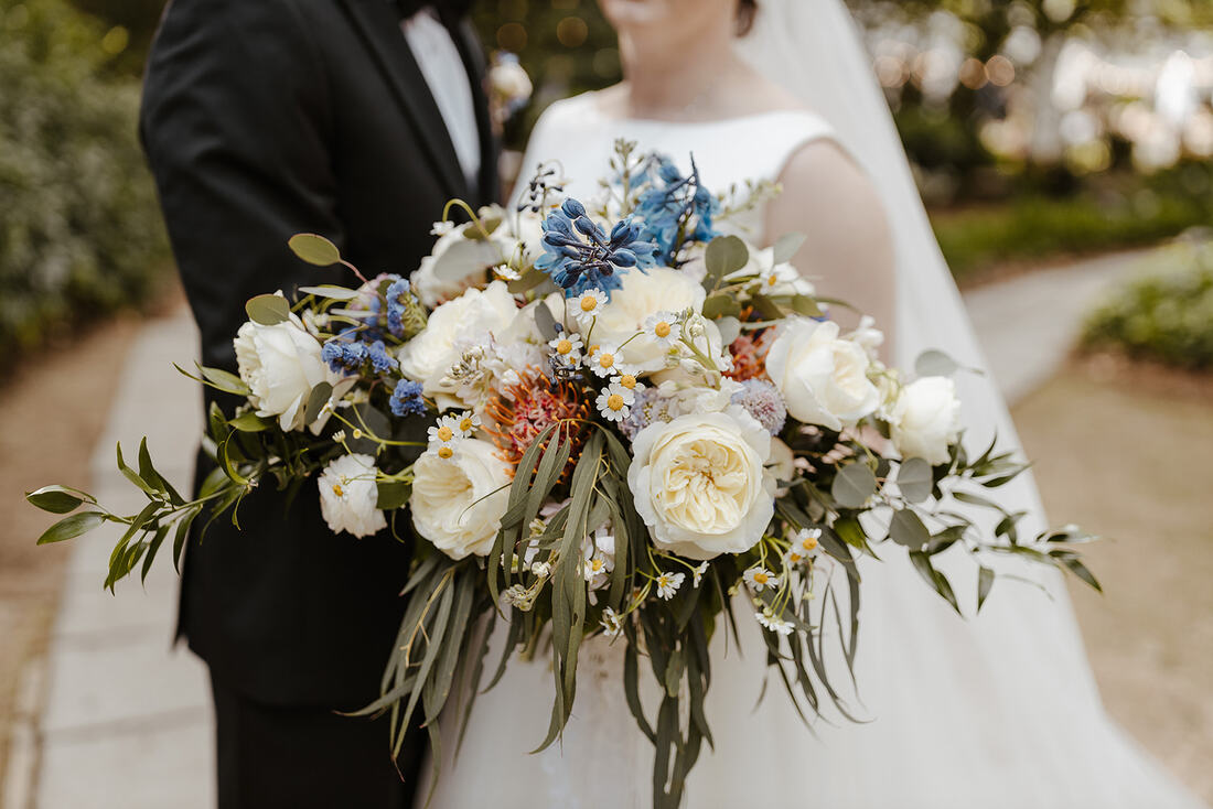 bride's bouquet with white, blue, and pink florals and draping greenery