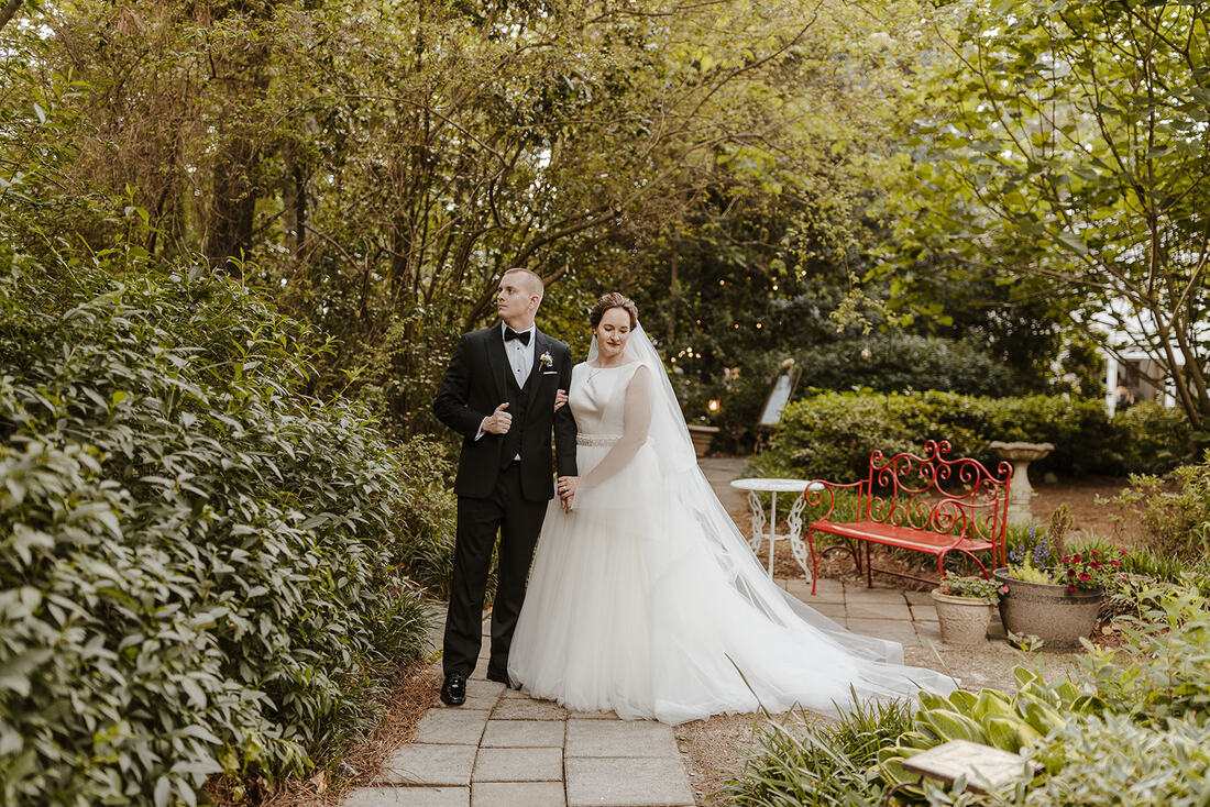 bride and groom posing along garden venue path looking away from each other