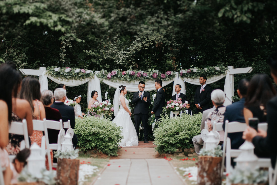 Wedding aisle and altar decorated with white chiffon and pops of pink flowers. White lanterns sit on stumps as pew markers.