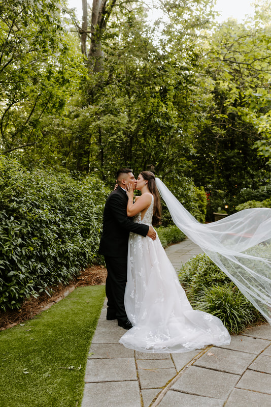 bride and groom kissing in garden with veil in air