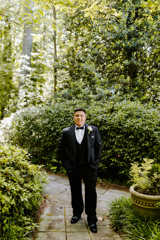 groom in black tux posing in garden venue