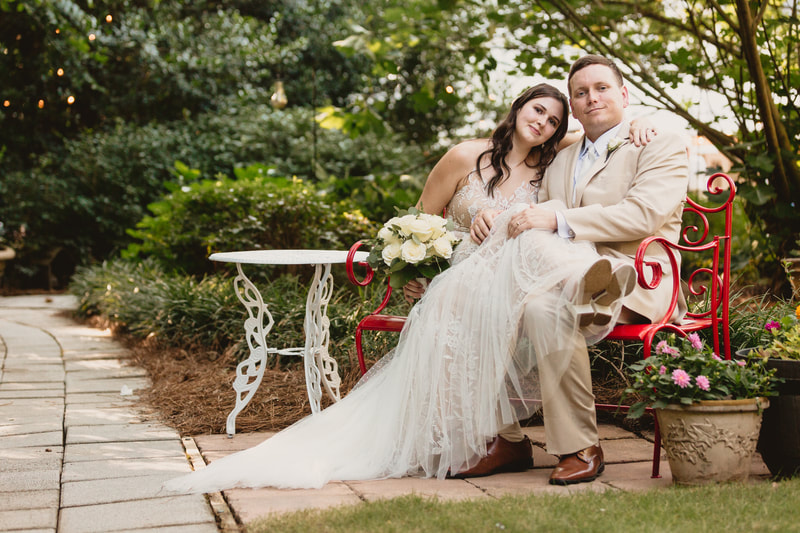 bride and groom posing on red iron bench on Four Oaks' grounds