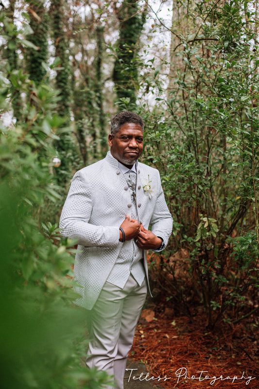 groom in silver suit standing in gardens