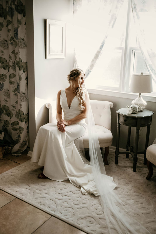Bride sitting on a white sofa chair in a bridal suite. 