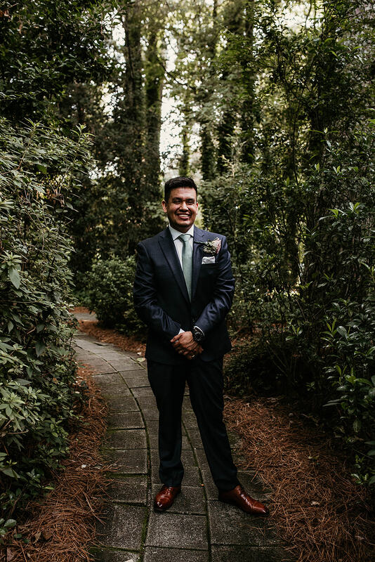 groom in navy suit posing in garden venue