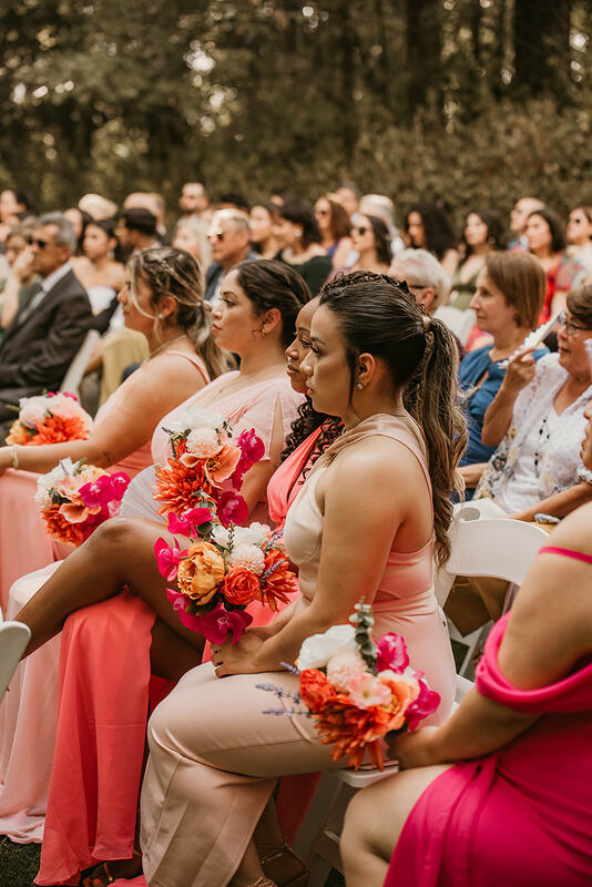 bridesmaids in shades of bright pink sitting with guests during ceremony