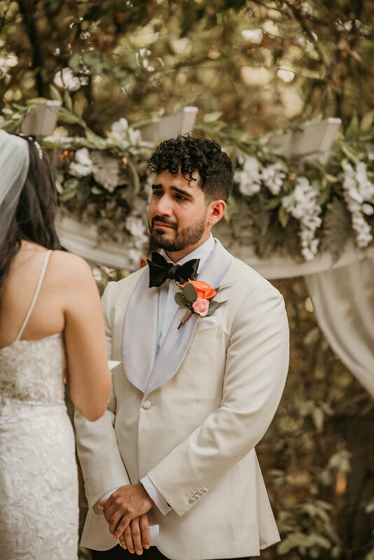 groom in white jacket looking at bride during vows