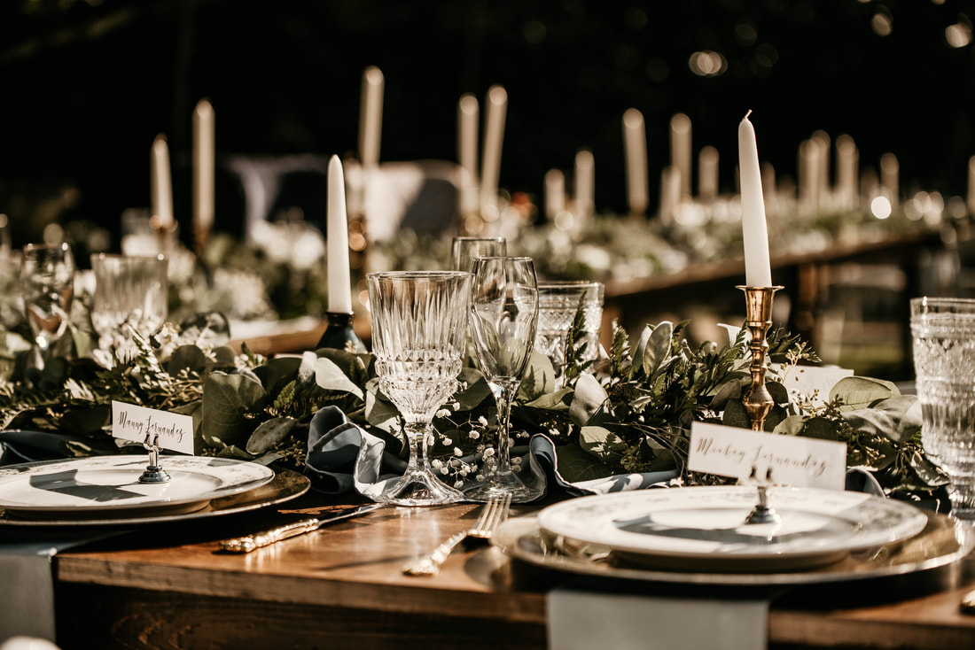 farm tables in u-shape decorated with greenery, gold candle sticks, and place settings
