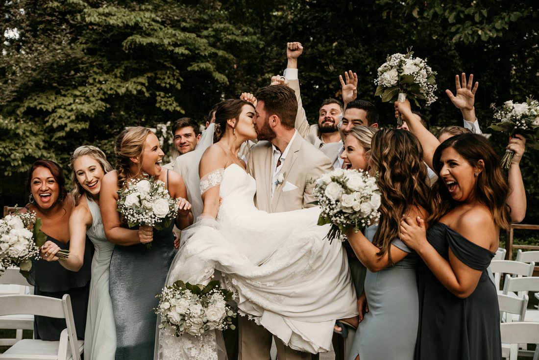 groom holding bride in arms as wedding party cheers