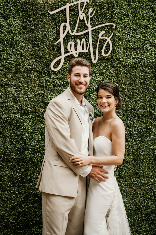 bride and groom in front of greenery wall with wooden 'the lants' sign