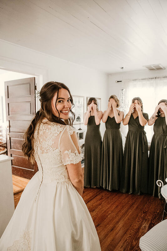 bride looking at camera while bridesmaids cover faces for reveal