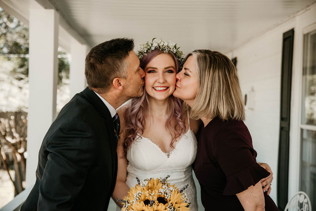parents kissing bride's cheeks on farmhouse porch