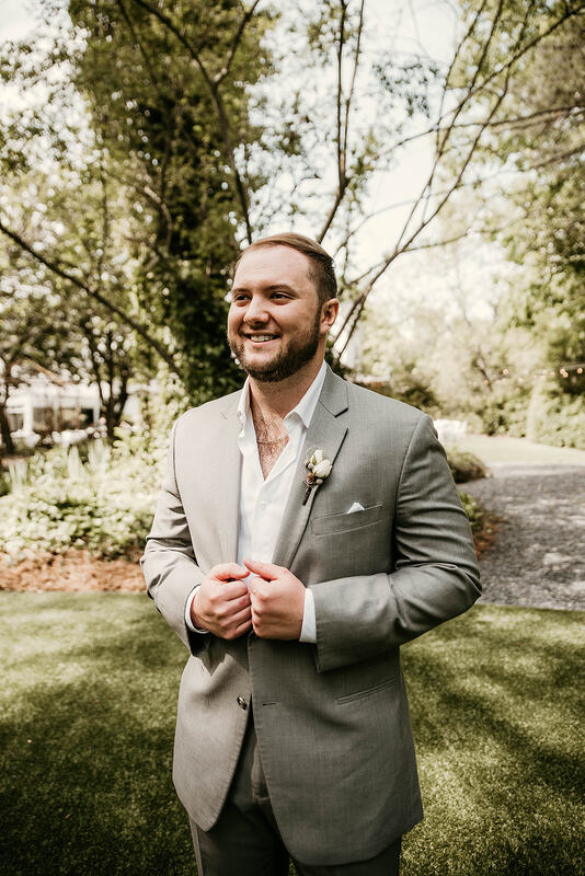 groom in gray suit posing in gardens