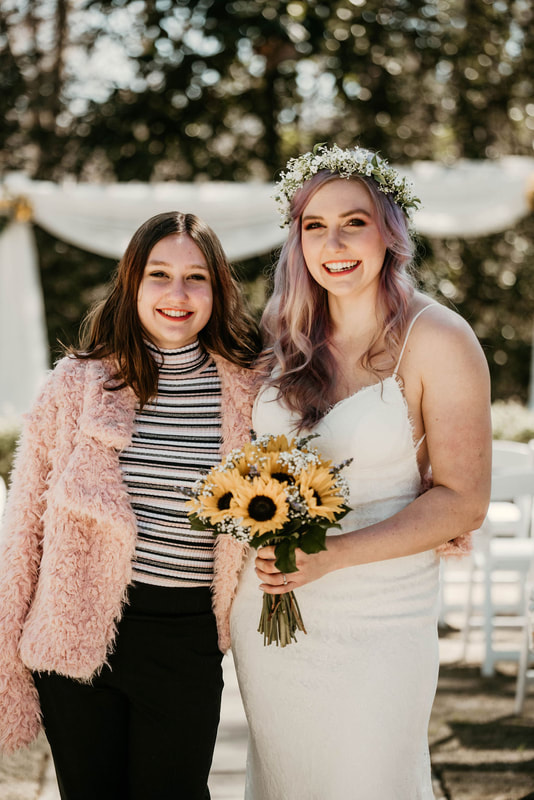 bride posing with sister in pink jacket by outdoor altar