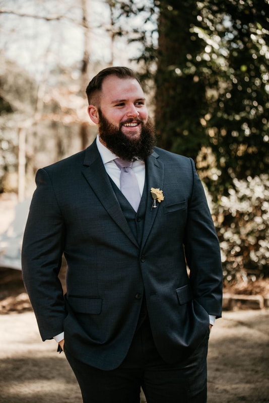 groom posing with hands in pockets by outdoor ceremony area
