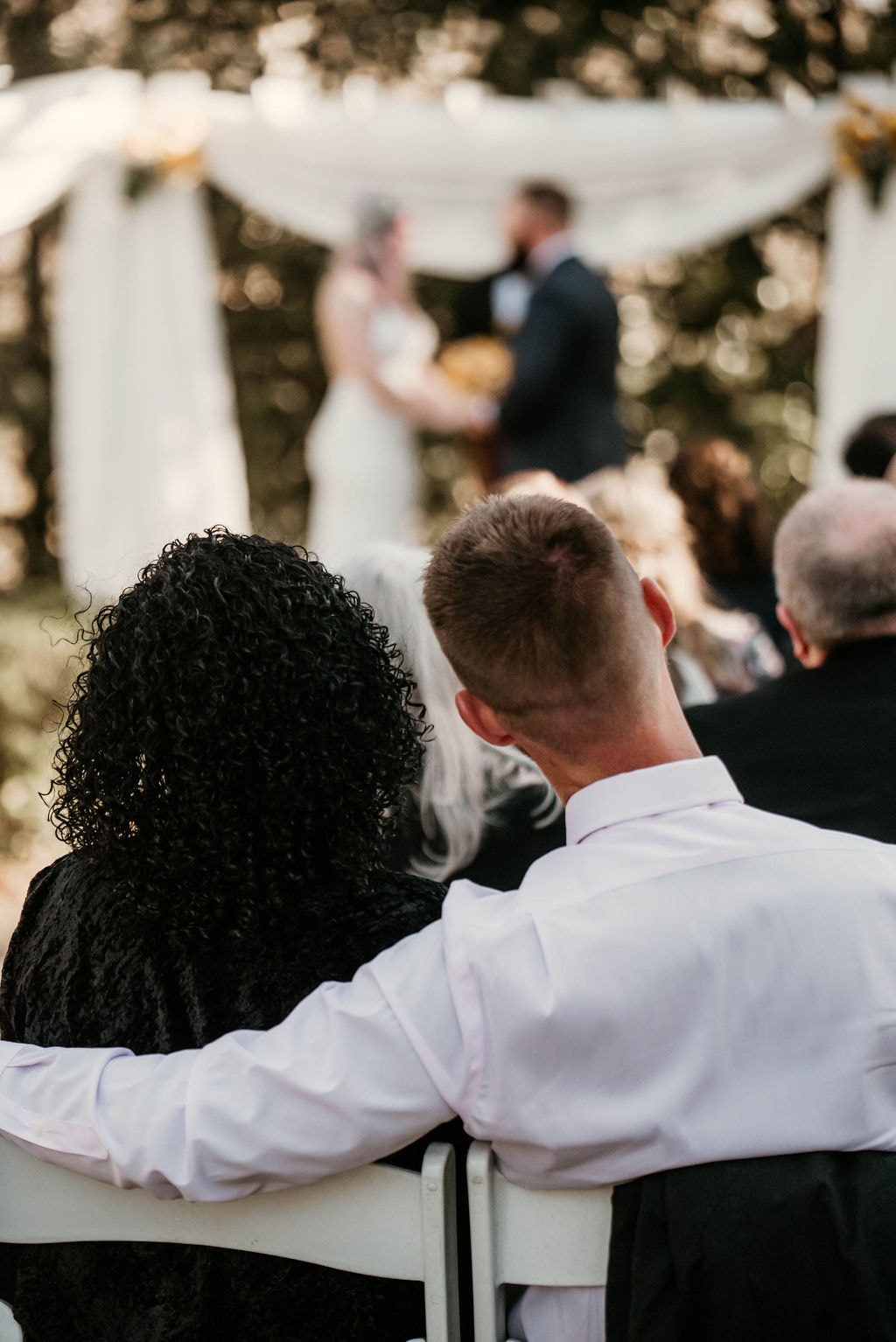 man with arm around woman while watching outdoor wedding ceremony