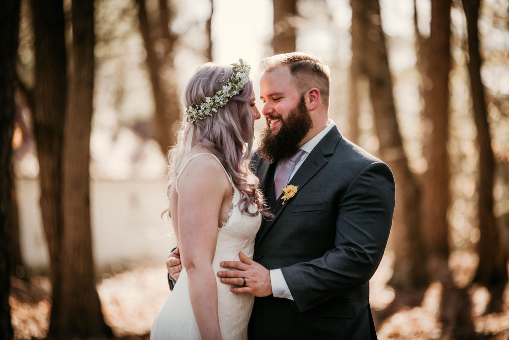bride in simple lace dress with lavender hair and flower crown standing with groom in charcoal suit