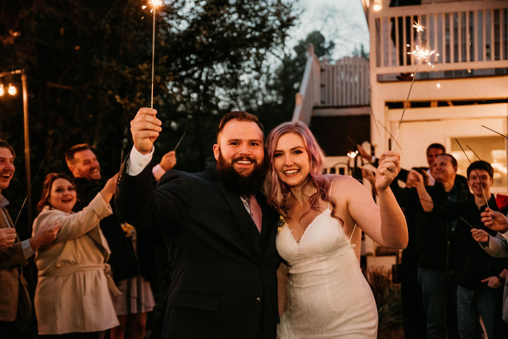 bride and groom holding sparklers with wedding guests