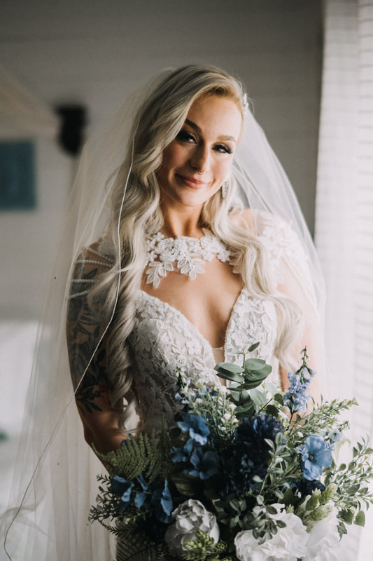 bride in lace dress holding blue bouquet in farmhouse bridal suite